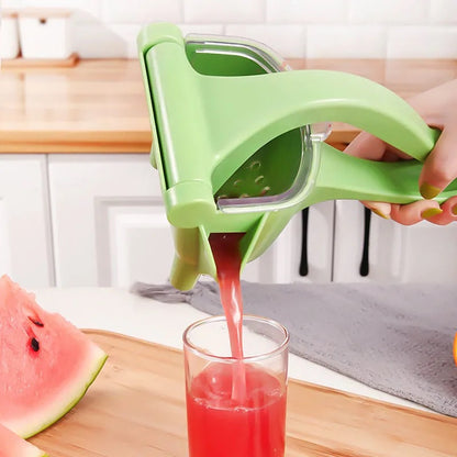 Green manual juicer squeezing watermelon juice into a glass on a kitchen counter.