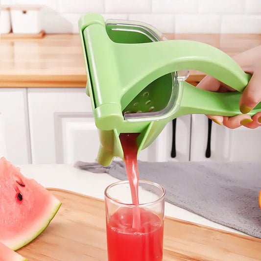 Green manual juicer squeezing watermelon juice into a glass on a kitchen counter.