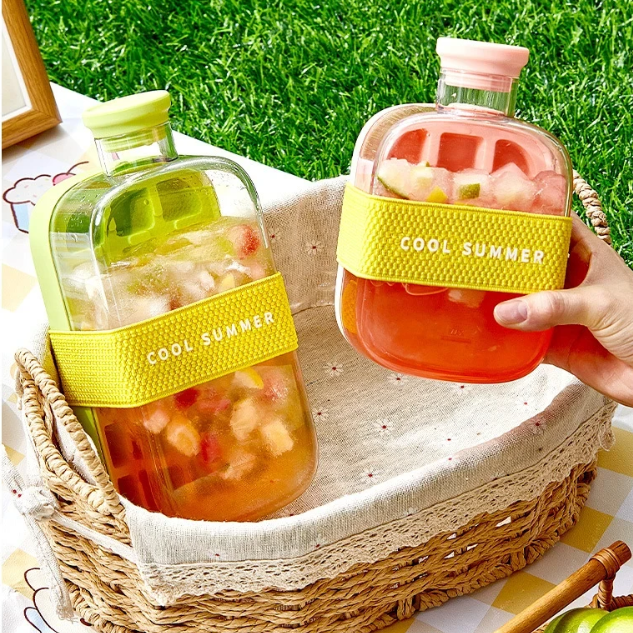 Two 'Cool Summer' Ice Cube Maker Jar drink bottles with colorful labels held by a hand against a grassy background.
